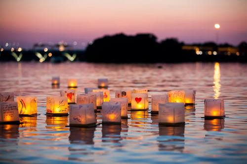 Floating lanterns with warm lights reflect on calm water at sunset, creating a serene and peaceful atmosphere.