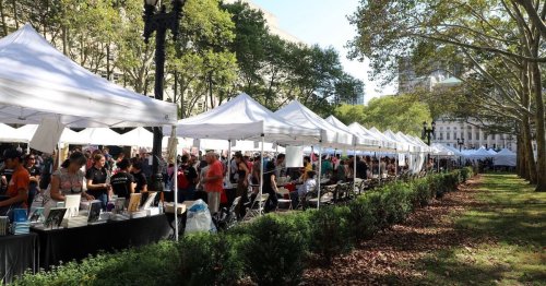 A bustling outdoor market with white tents, people browsing, and trees lining the pathway.