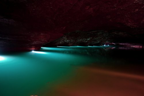 A serene underground cave with glowing blue-green water and subtle lighting reflecting off the rocky ceiling.