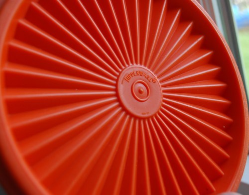 Close-up of a bright orange Tupperware lid with a sunburst design and the Tupperware logo in the center.