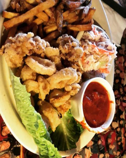 A plate of fried calamari with fries, coleslaw, lettuce, and marinara sauce on the side.