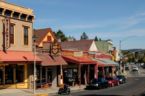 Historic storefronts line a street in a small town, featuring shops and a clear blue sky overhead.