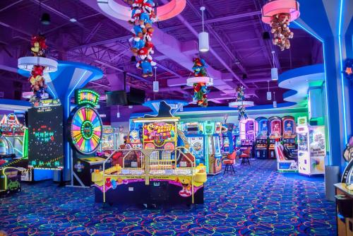 Brightly lit arcade with colorful games, a spinning wheel, and plush toys hanging from the ceiling.