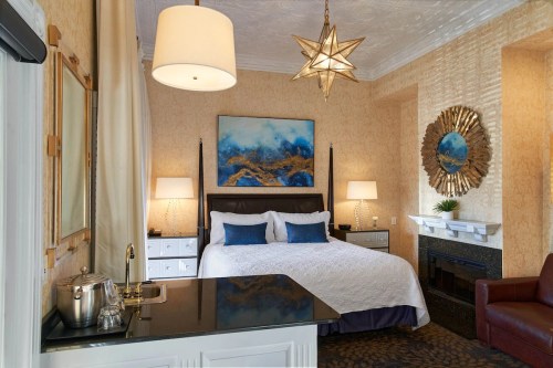 Cozy hotel room with a king bed, decorative artwork, a fireplace, and stylish lighting fixtures.