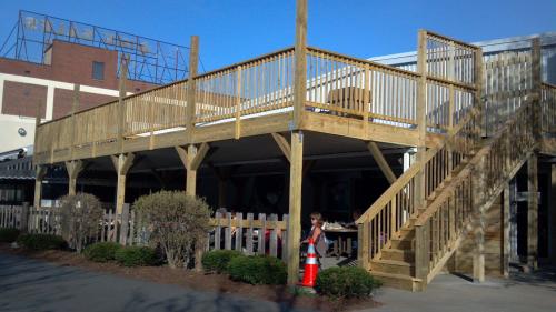 A wooden deck with stairs, surrounded by bushes, next to a building. A child stands near a traffic cone.