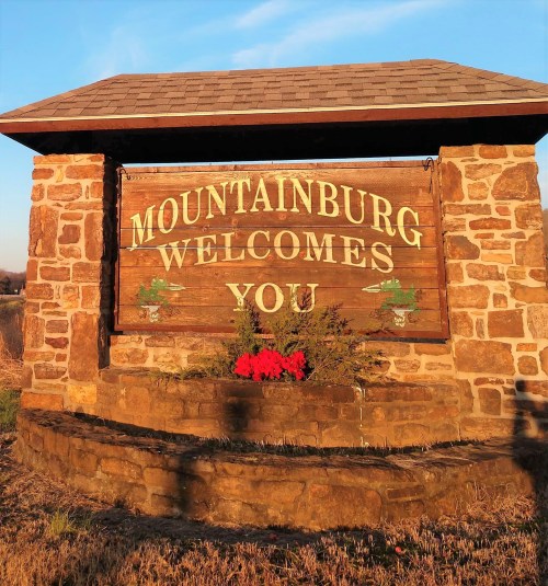 A stone welcome sign for Mountainburg, featuring the text "Mountainburg Welcomes You" and decorative plants.