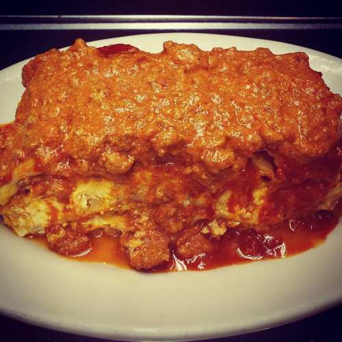 A hearty serving of lasagna topped with a rich meat sauce on a white plate.