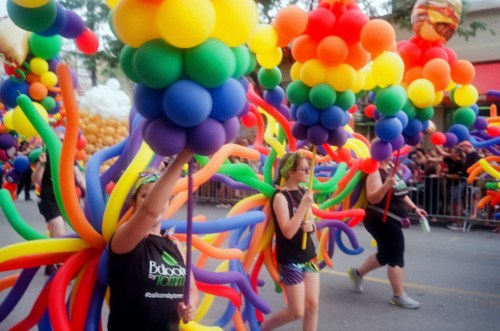 Participants in a parade hold colorful balloon creations, celebrating with vibrant decorations and festive attire.