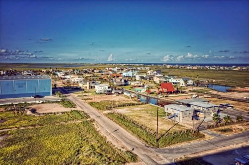 Aerial view of a coastal town with houses, roads, and waterways under a clear blue sky.