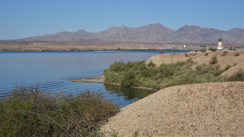 A serene lake with gentle waves, surrounded by sandy shores and distant mountains under a clear blue sky.