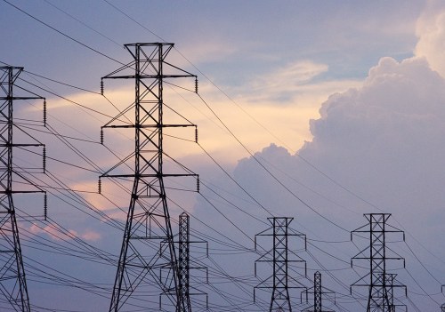 Silhouettes of power lines and towers against a colorful sky with clouds at sunset.
