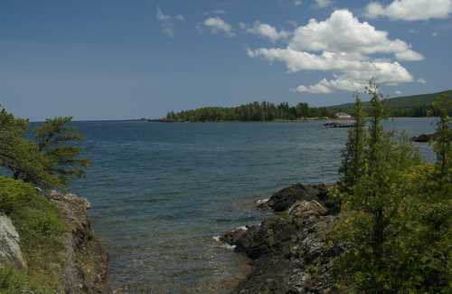 A serene coastal view featuring rocky shores, clear blue water, and lush green islands under a partly cloudy sky.