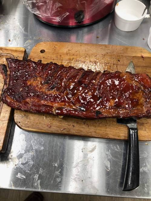A glazed rack of ribs on a wooden cutting board, with a knife resting beside it.