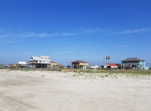 Colorful beach houses on stilts line a sandy shore under a clear blue sky.