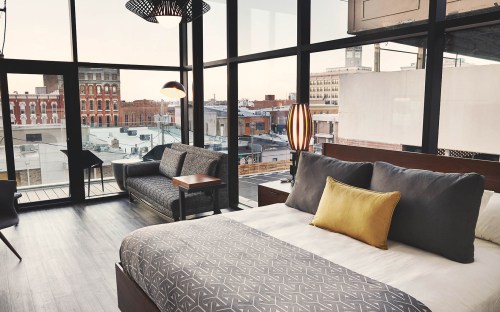 A modern hotel room with a large window view, featuring a bed, sofa, and stylish decor.