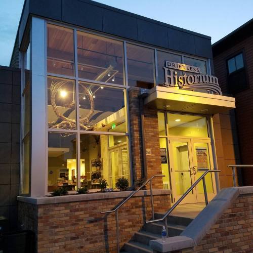 Exterior view of the Driftless Historium building, featuring large windows and a welcoming entrance at dusk.