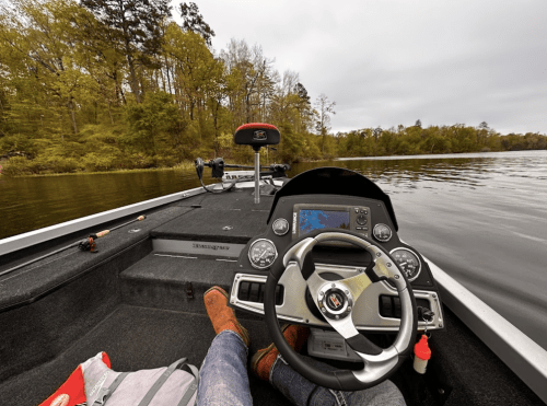 A view from the front of a boat, showing the steering wheel and dashboard, with a person’s feet resting on the deck.