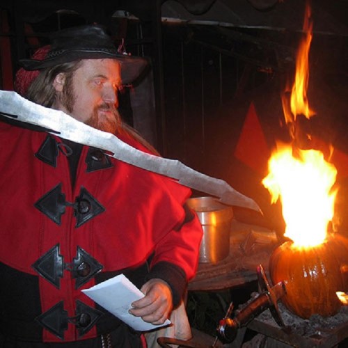 A man in a red coat holds a sword near a flaming pumpkin, creating a dramatic and festive atmosphere.