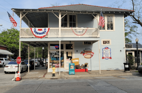A blue building with a porch, decorated with flags and bunting, featuring an ice cream shop and a "Stop" sign outside.
