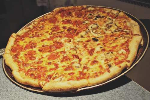 A large pizza on a tray, half topped with pepperoni and half with mushrooms and cheese.