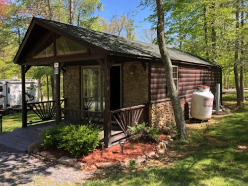 A cozy cabin with a stone and wood exterior, surrounded by greenery and featuring a small porch.