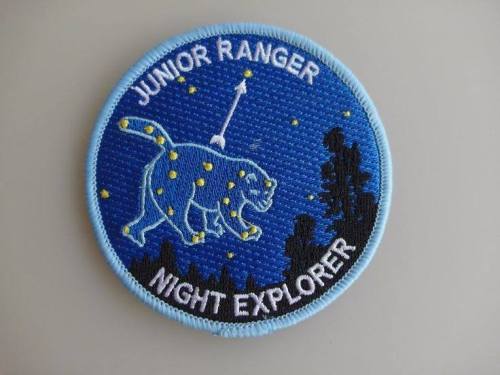 A circular patch featuring a blue background, a cat silhouette, stars, and the text "Junior Ranger Night Explorer."