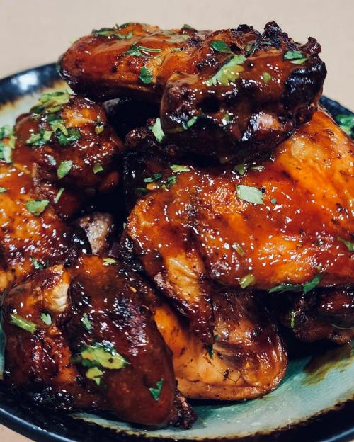 A close-up of glazed chicken wings garnished with fresh herbs on a decorative plate.