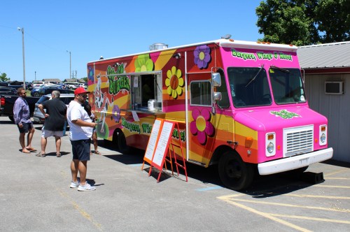 A colorful food truck with flower designs, serving customers in a sunny outdoor setting.