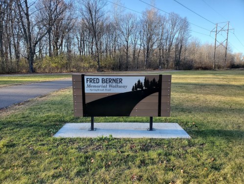 Sign for Fred Berner Memorial Walkway in Springfield, Texas, surrounded by trees and open grass.