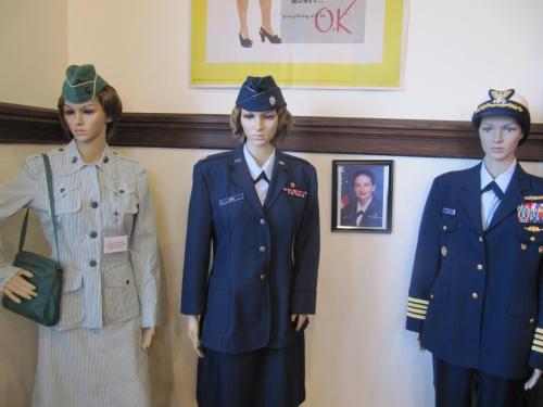 Three mannequins display military uniforms: a vintage green outfit, a navy uniform, and an air force dress uniform.