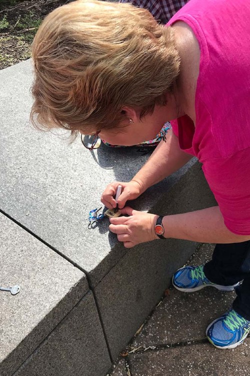 A woman with short hair is drawing on a stone surface while wearing a pink shirt and blue sneakers.