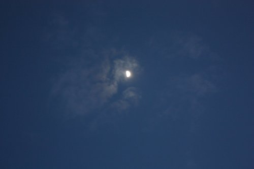 A crescent moon partially obscured by wispy clouds against a deep blue sky.