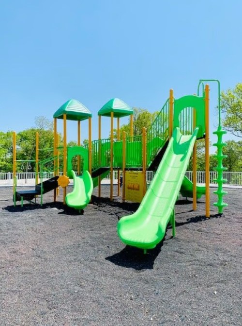 Bright green playground equipment with slides and climbing structures on a sunny day. Black rubber surface below.