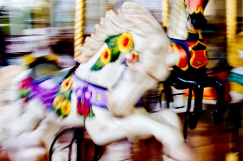 A blurred image of colorful carousel horses in motion, showcasing vibrant floral designs.
