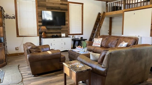 Cozy living room with leather sofas, a TV, wooden accents, and a lofted area, featuring warm, inviting decor.