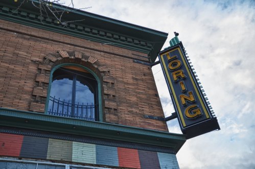 A vintage brick building with a large "LORING" sign and a decorative window under a cloudy sky.