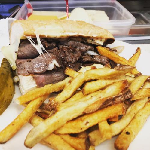 A hearty sandwich filled with sliced beef and melted cheese, served with crispy fries and a pickle on the side.