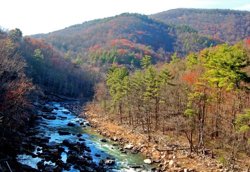 A serene river flows through a forested valley, with colorful autumn foliage on the surrounding hills.