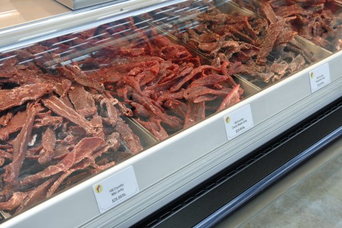 Display of various types of jerky in a refrigerated case, with price tags visible.