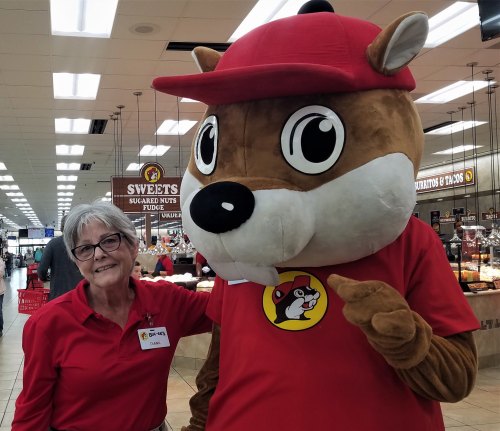 A woman in a red shirt poses with a large, friendly mascot in a store, both smiling at the camera.