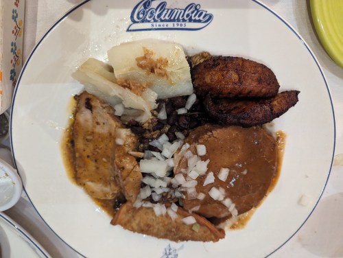 A plate of Colombian food featuring chicken, plantains, yuca, black beans, and onions, served on a decorative dish.