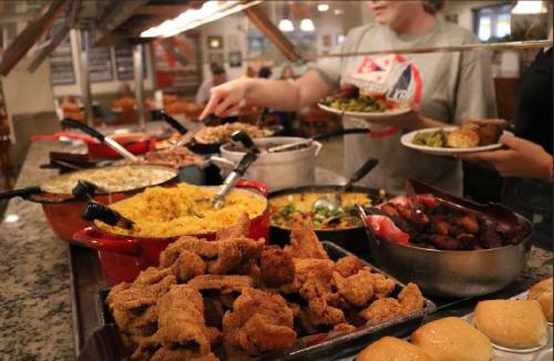 A buffet spread featuring fried chicken, sides, and rolls, with diners serving themselves in a cozy restaurant setting.