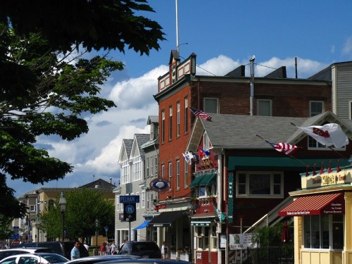 Colorful buildings line a street under a blue sky with clouds, featuring flags and storefronts.
