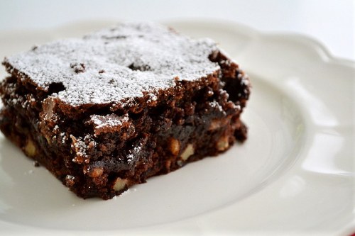 A square piece of chocolate brownie dusted with powdered sugar on a white plate.