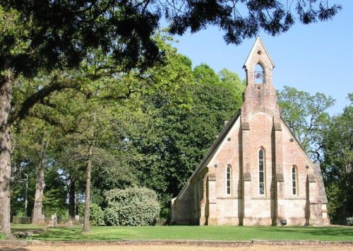 A quaint brick church with a steeple, surrounded by lush green trees and a peaceful landscape.