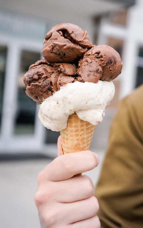 A hand holding a cone with three scoops of chocolate ice cream and one scoop of vanilla.