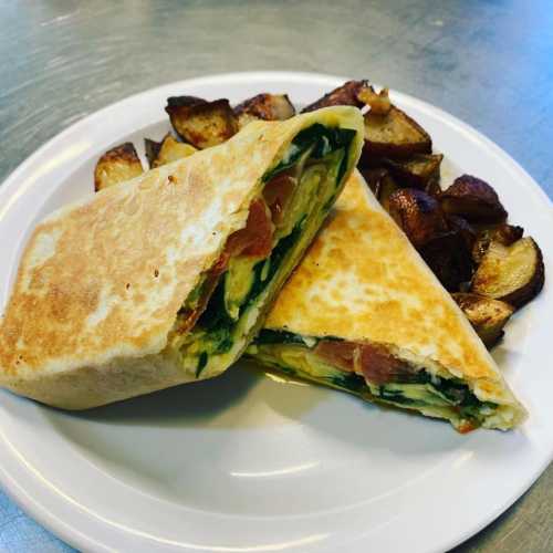 A plate with a folded wrap filled with spinach, tomatoes, and bacon, accompanied by golden-brown roasted potatoes.