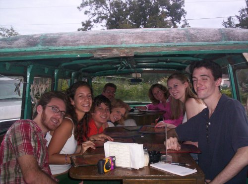 A group of eight friends sitting together in a vintage vehicle, smiling and enjoying a meal.