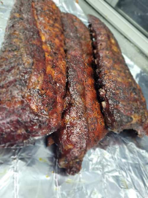 Three succulent, smoked ribs glistening with a rich, dark glaze, resting on aluminum foil.