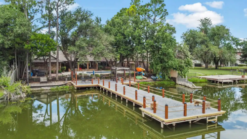 A serene lakeside view featuring a wooden dock, lush trees, and a cozy cabin in the background.
